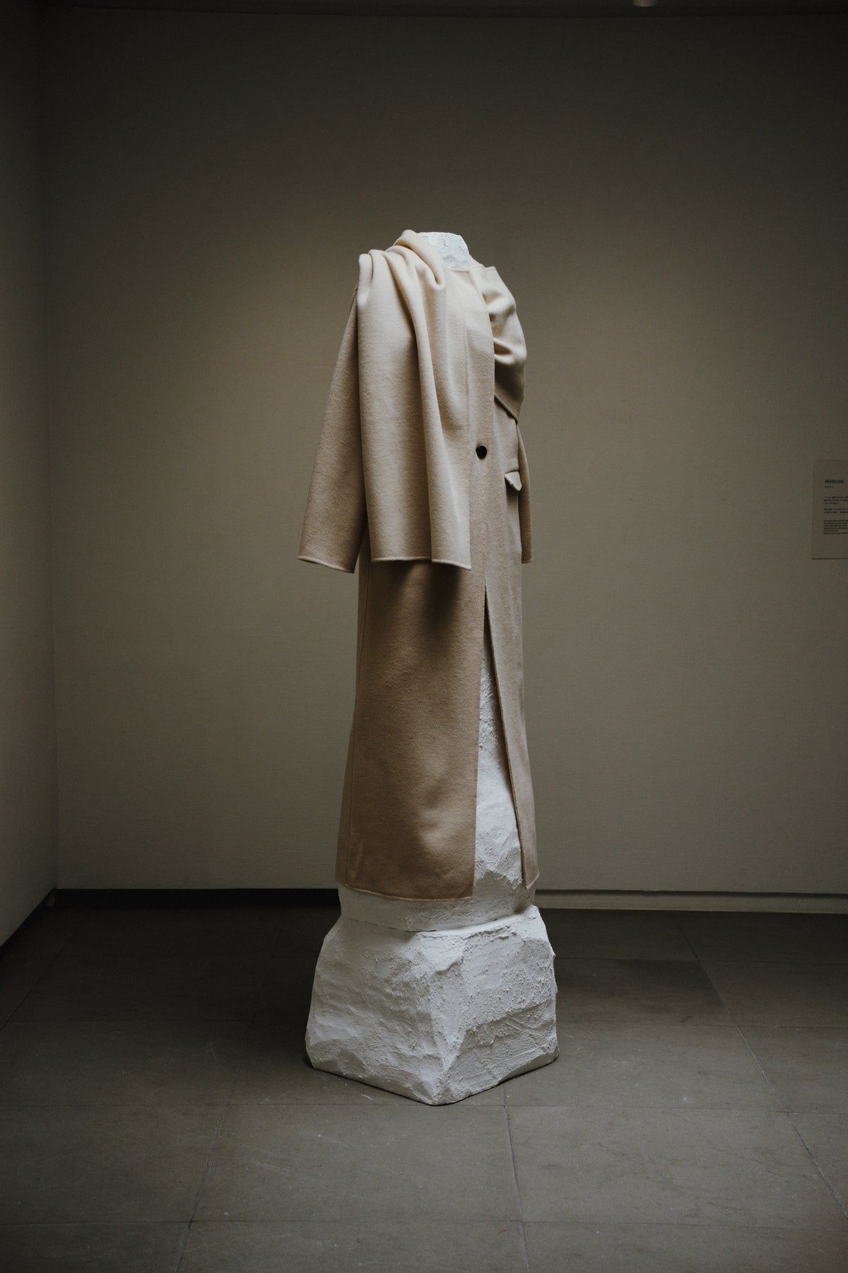 白い彫刻の台座に展示されたベージュの衣服。